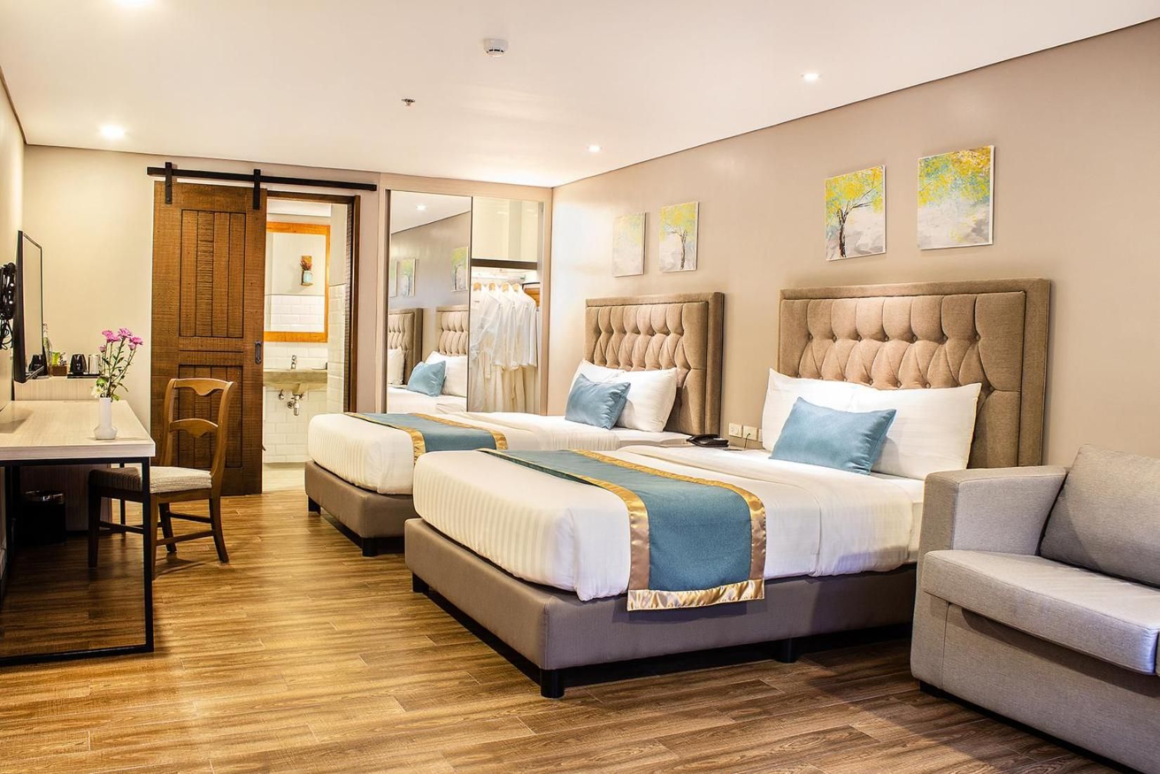 A hotel room with two beds, a sofa, a dining table, and a mirror.