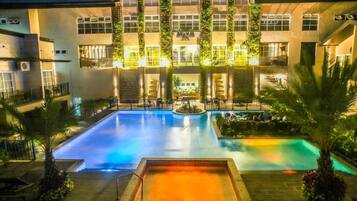 A hotel with a swimming pool, multiple balconies, and a well-lit exterior.