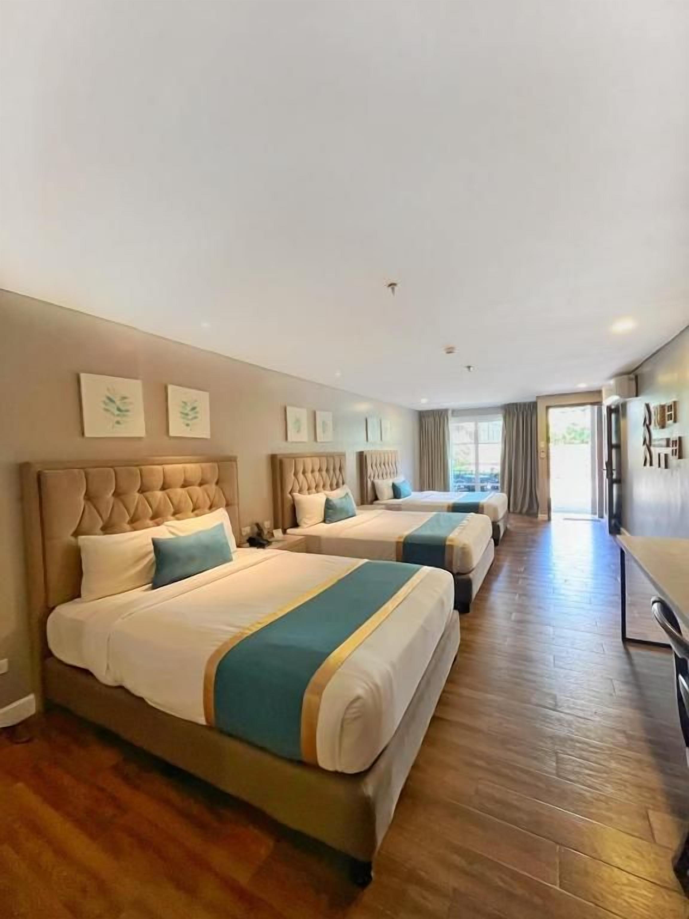 A hotel room with two beds, a wooden floor, a kitchenette, and a view of the outdoors.