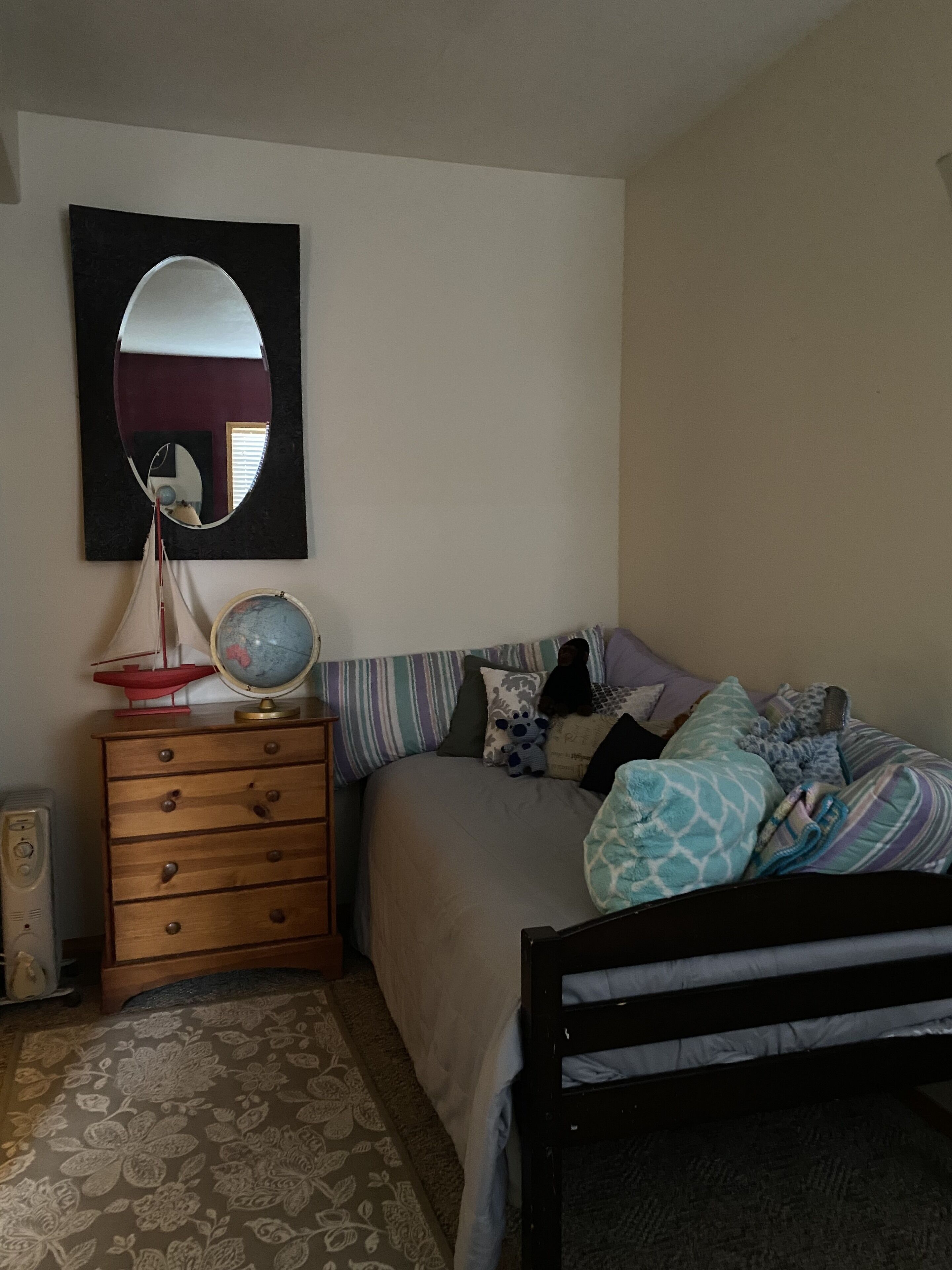 Une chambre à coucher avec un lit, une commode, un miroir, un globe terrestre et une maquette de bateau.