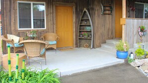 A wooden cabin with a porch, wicker chairs, a blue planter, and a bird figurine. - A Home With Room to Roam (Omak)