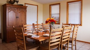 A dining room with a wooden table set for six, surrounded by wooden chairs. A wooden cabinet is to the left, and there is a window with blinds on the right. - A Home With Room to Roam (Omak)