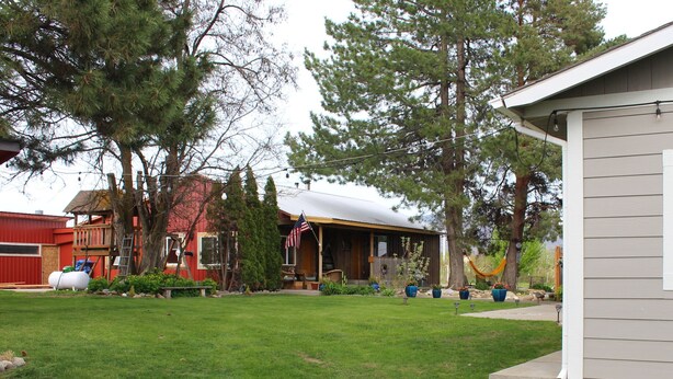 A residential property with a well-maintained lawn, a wooden deck, and a house with a porch. - A Home With Room to Roam (Omak)