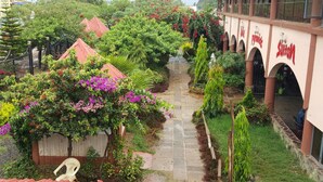 A courtyard with a pathway, surrounded by lush greenery and a building with arched windows. - Sultan Hamud Pyramids Resort (Sultan Hamud)