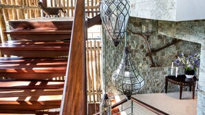Una escalera de madera con barandilla de metal, pared de piedra y faroles colgantes.
