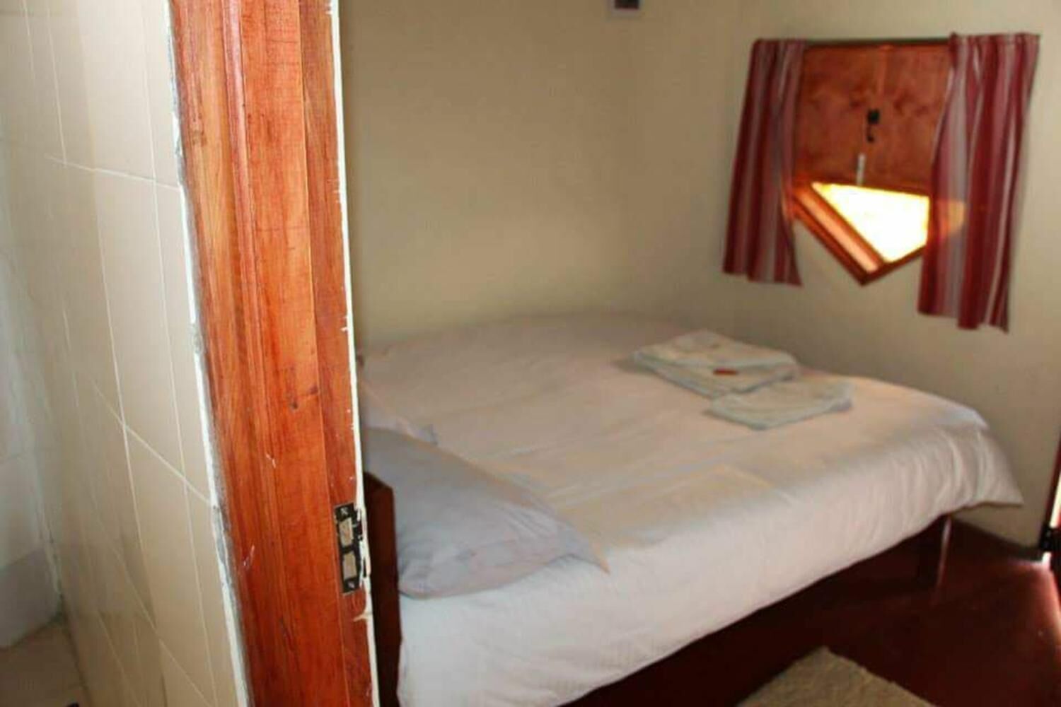 Un lit simple avec du linge de lit blanc, un cadre de porte en bois et un luminaire fixé au mur.