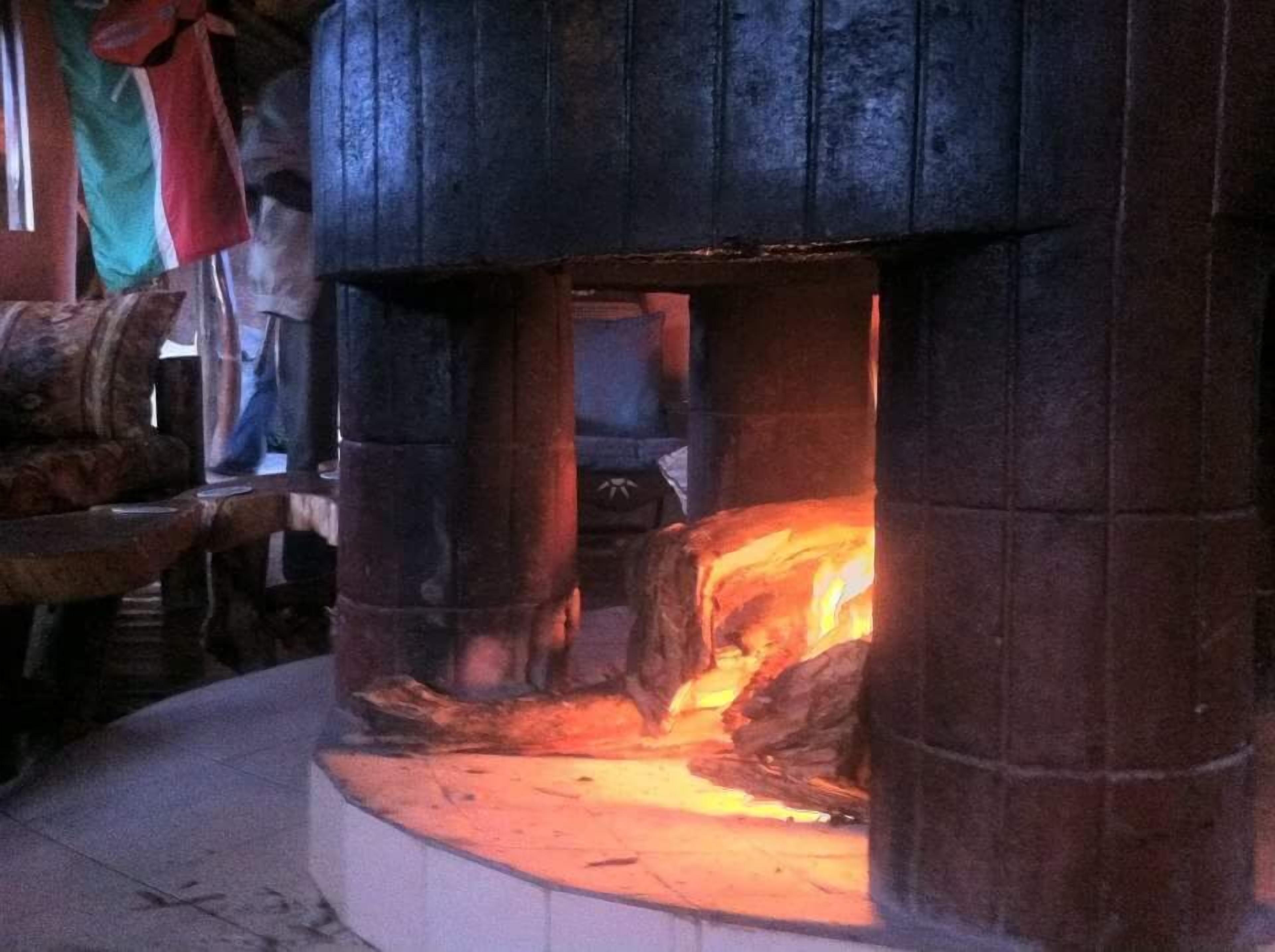A stone fireplace with a fire burning inside, surrounded by wooden logs and a rustic interior.