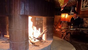 Una chimenea de piedra con fuego encendido, rodeada de suelo de baldosas y muebles de madera.
