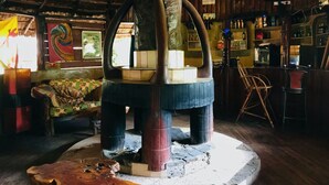 Un interior rústico con techo de madera, una estructura central de madera que recuerda a un árbol, y una zona de bar con estantes y botellas.