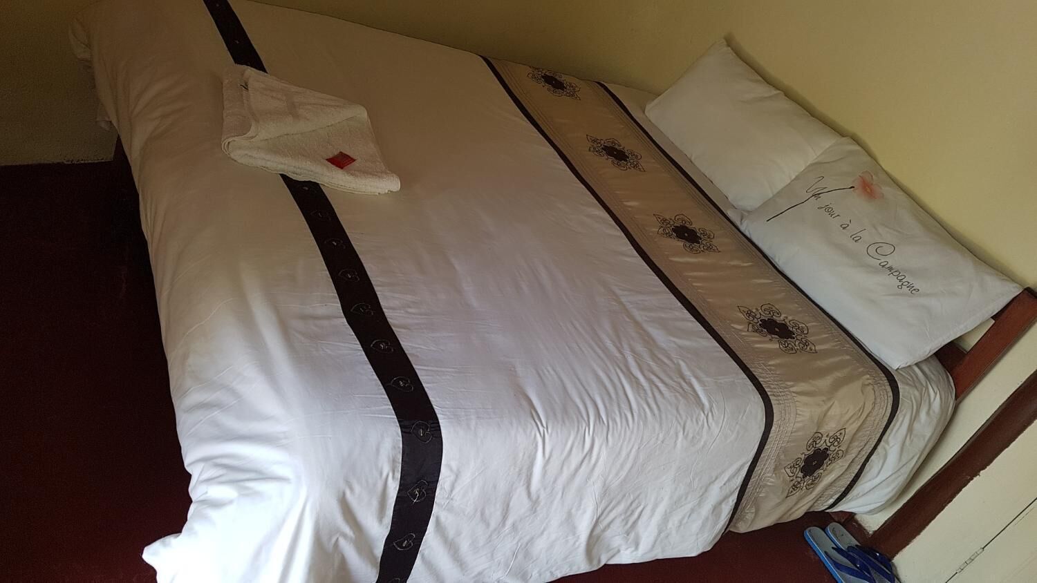 A hotel room with a large bed, a white and black striped headboard, and a decorative pillow with text.