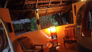 Una habitación acogedora con techo de paja, una silla de madera, una mesa con lámpara y vistas al exterior.