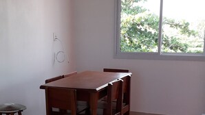 A dining area with a wooden table and chairs, a small stool, and a window with a view of greenery. - 03 Apartments for Vacation - Morada Madruga - Sea Front, Superior (Praia do Sonho (Ens Brito))