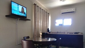 Ein Essbereich mit rundem Tisch und Stühlen, einem an der Wand befestigten Fernseher, einem Fenster mit Aussicht und einer Klimaanlage.