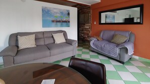 Ein Wohnzimmer mit zwei Sofas, einem Esstisch und einem Gemälde mit Strandmotiv.