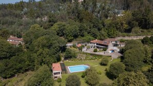 An aerial view of a residential area with a swimming pool, multiple houses, and dense surrounding trees.