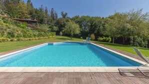A rectangular swimming pool with a wooden deck in the foreground, surrounded by a well-maintained lawn and trees.
