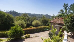 A stone building with a tiled roof, surrounded by lush greenery and a clear view of a hilly landscape.