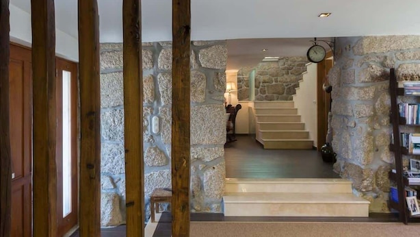 A stone-walled staircase leading to a second floor, with a wooden door frame on the left and a bookshelf on the right.