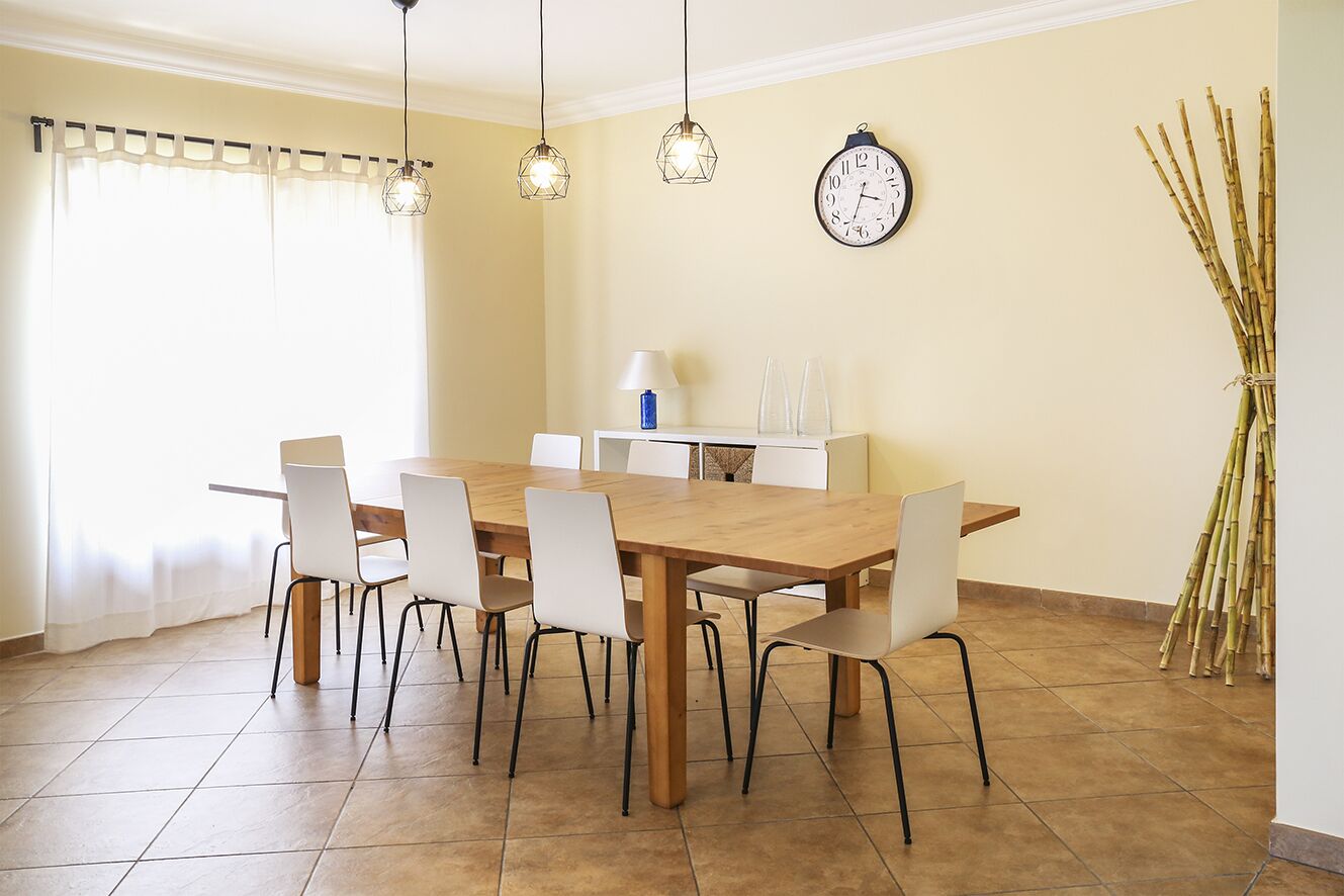 Un coin repas avec une table en bois et des chaises blanches, une horloge au mur et une décoration en bambou.