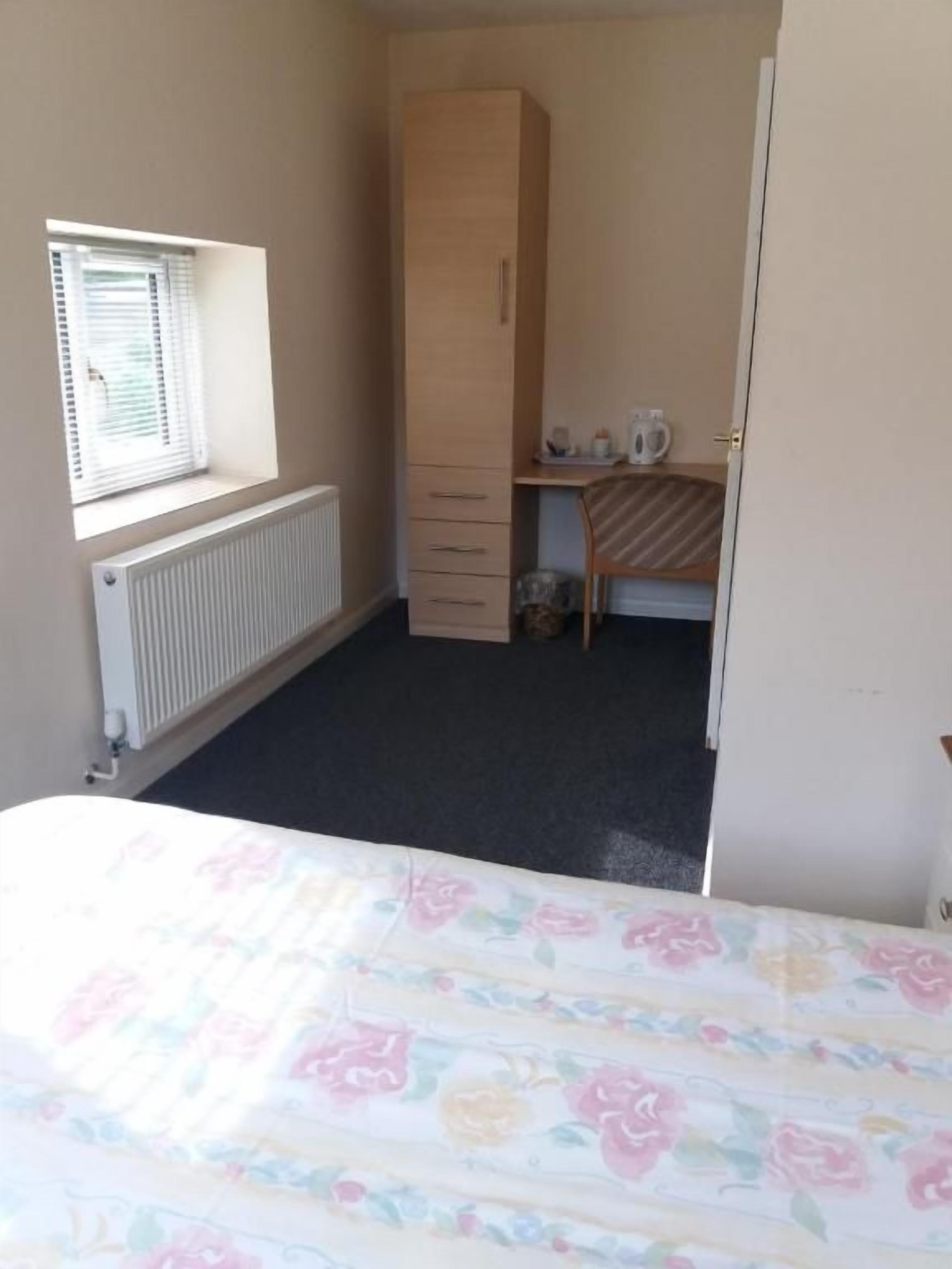 A bedroom with a bed, a wardrobe, a radiator, and a window with blinds.