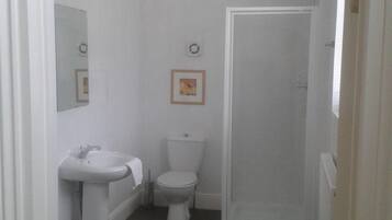Un baño pequeño y estrecho con un lavabo, inodoro y cabina de ducha, todos de color blanco.