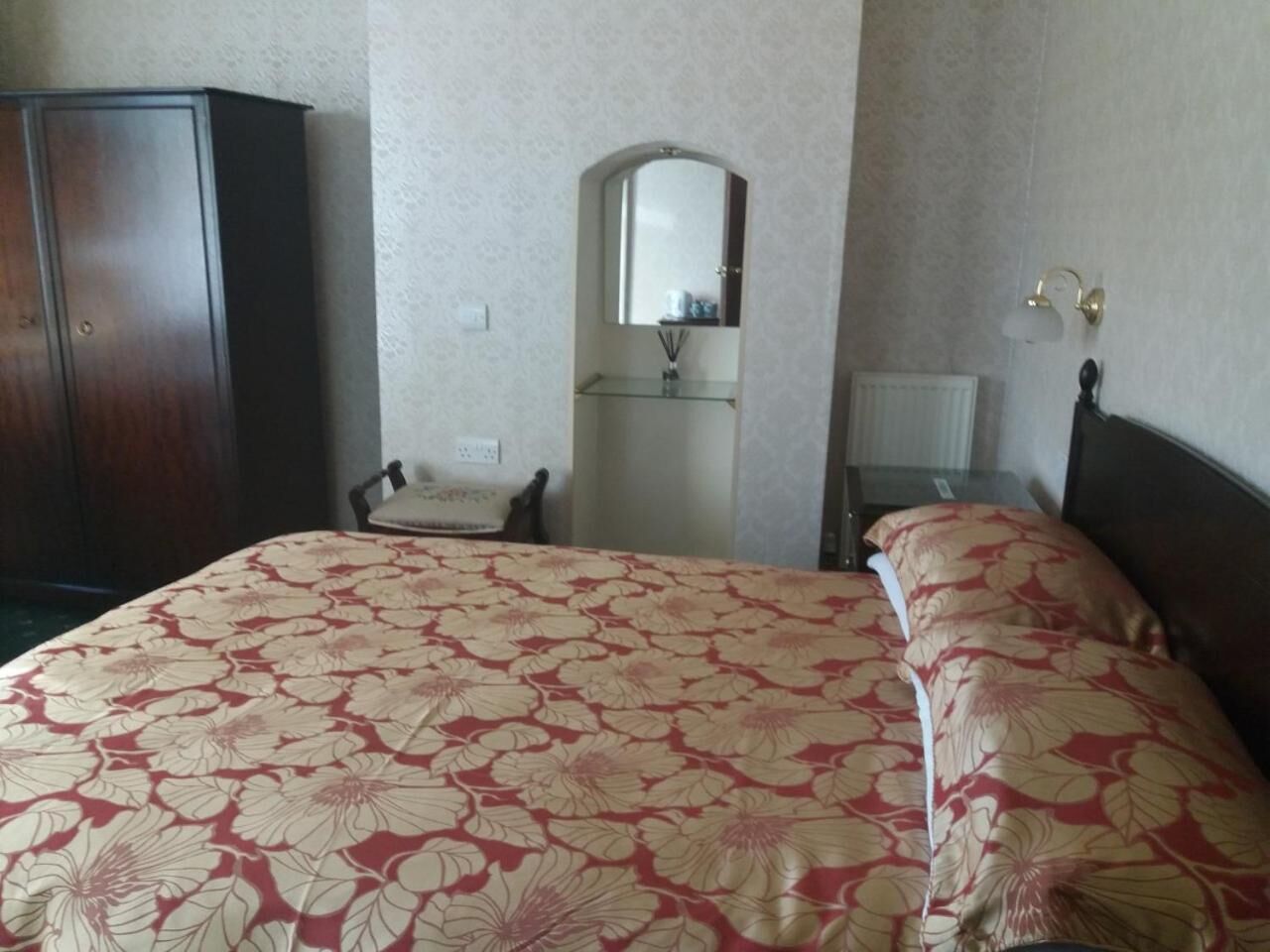 Un dormitorio con cama, una silla, un armario, un espejo y una mesita de noche.