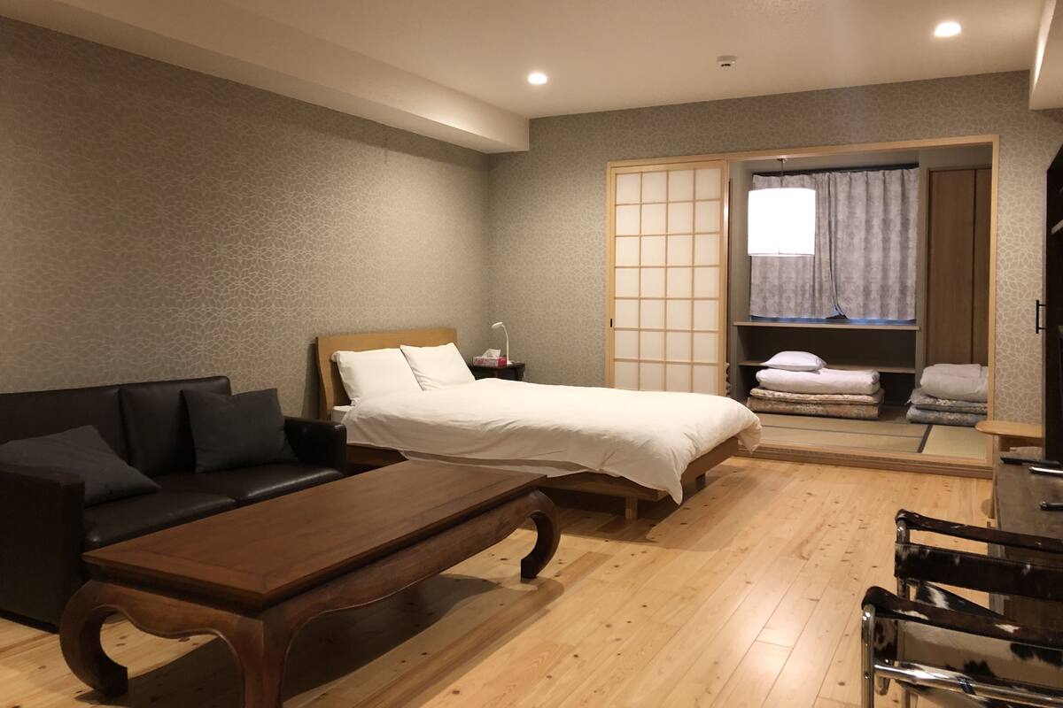A hotel room with a bed, a sofa, a wooden table, and a sliding door leading to a bathroom.