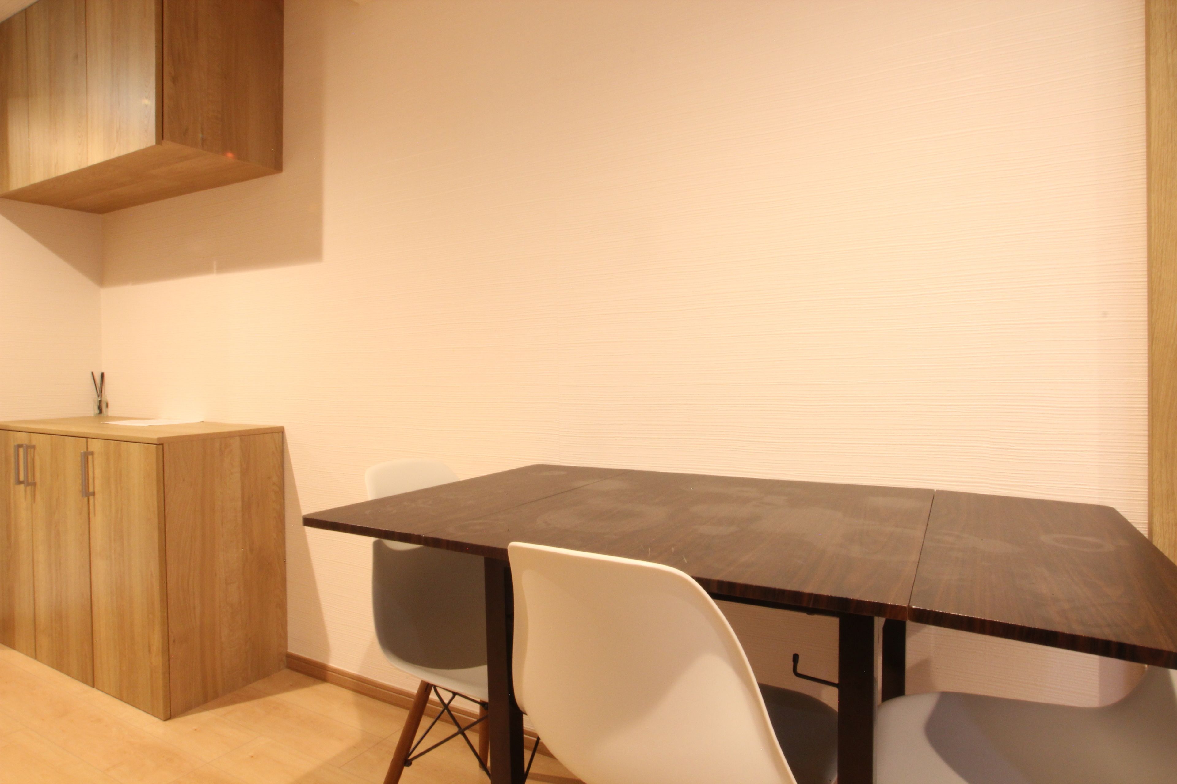 A small, modern kitchen with a wooden cabinet, a dark wooden table, and white chairs.