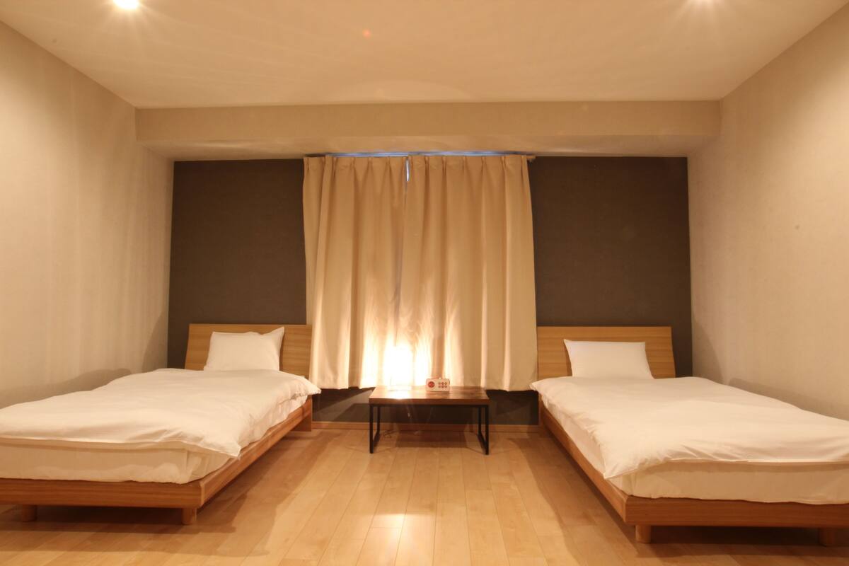 A room with two single beds, a small table, and a curtain.