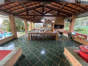 Un'ampia area cucina esterna con un bancone, circondata da una piscina e un patio.
