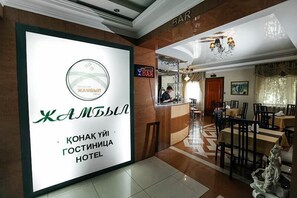 A hotel lobby with a reception desk, a bar area, and dining tables. - Hotel Zhambyl (Taraz)