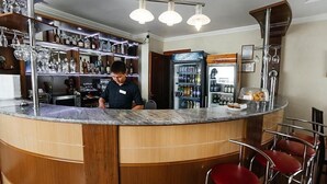 Un espace bar doté d’un comptoir en marbre, d’étagères en bois où sont disposées des bouteilles, et d’un réfrigérateur rempli de boissons.