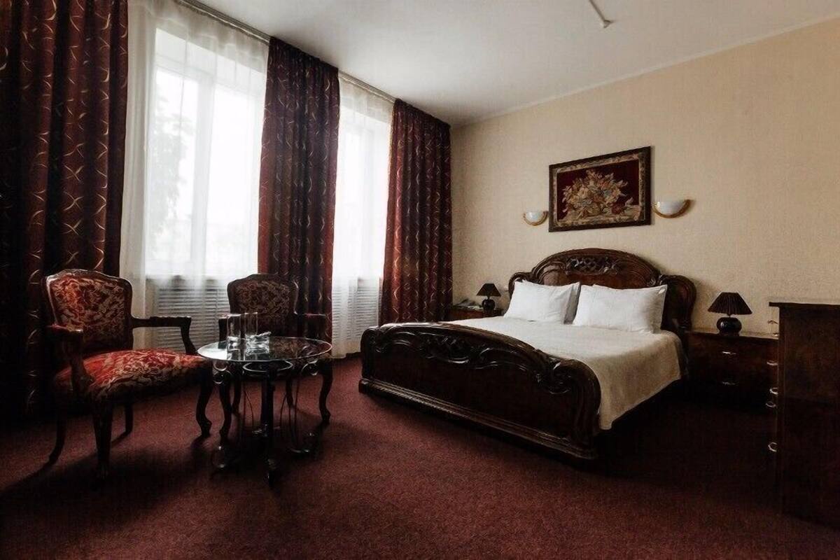 Una habitación de hotel con una cama grande, dos sillas, una mesita pequeña y una mesita de noche con lámparas.