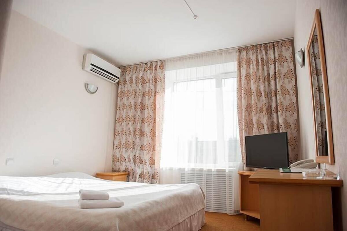 Habitación de hotel con cama, escritorio con televisor y ventana con cortinas florales.