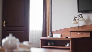Une chambre d’hôtel avec un bureau en bois, une lampe, une théière et une fenêtre avec des stores.