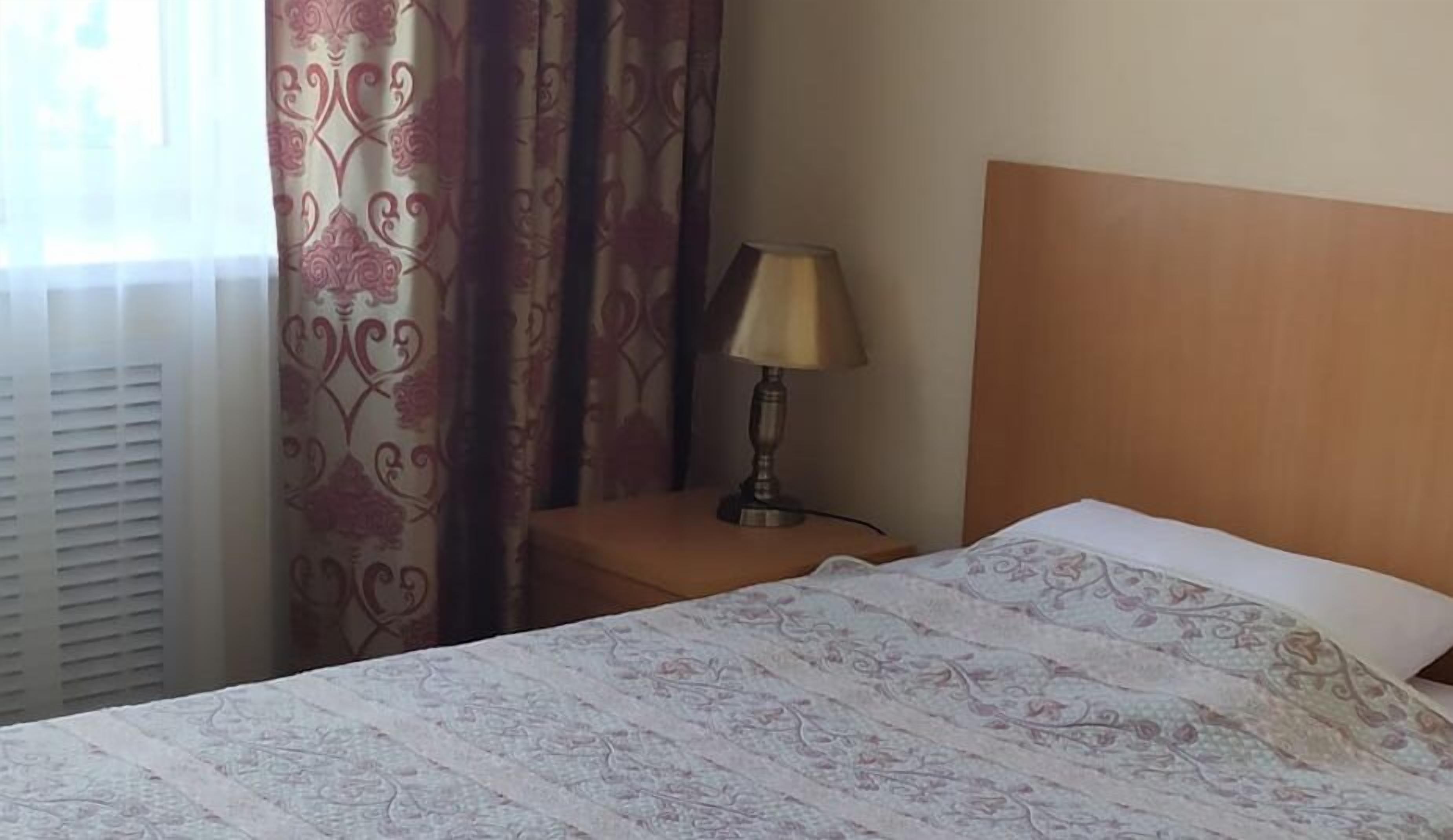 A hotel room with a bed, a nightstand with a lamp, and patterned curtains.