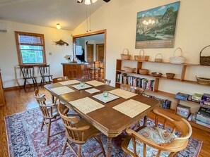 A dining room with a wooden table, chairs, a rug, and a bookshelf with baskets.