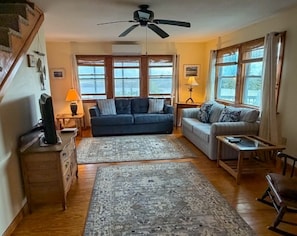 A living room with a sofa, a coffee table, a rug, a ceiling fan, and a staircase.