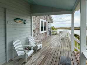 A wooden deck with Adirondack chairs, a fish decoration, and a view of the water.