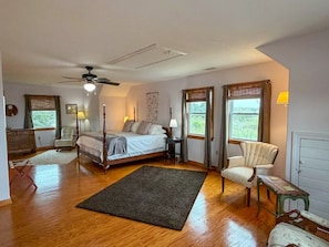 A bedroom with a four-poster bed, a ceiling fan, a desk, and a chair.