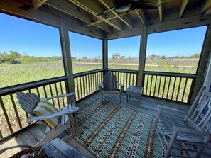 Une véranda couverte avec des balustrades en bois, deux fauteuils Adirondack, une petite table et un tapis à motifs.