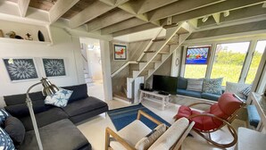 A living room with a sofa, a chair, a coffee table, a TV, and a staircase. - Mosby's Manor:  Eclectic design, unique interior, distant sound views. (Ocracoke)