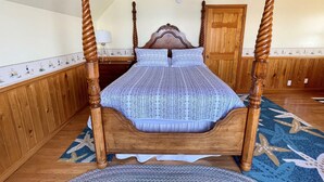 Ein Himmelbett mit gemustertem Überwurf, Holzwände, einer Holztür und einem Deckenventilator.