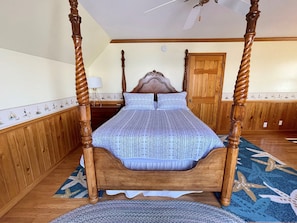 A four-poster bed with a patterned bedspread, wooden walls, a wooden door, and a ceiling fan.