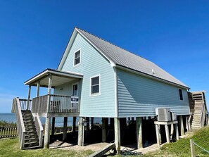 A light blue wooden house with a balcony, a porch, and a staircase leading to the main floor.