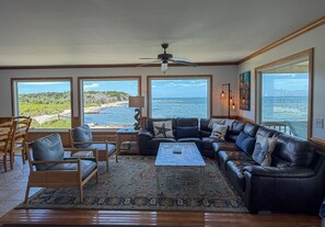 A living room with a view of the ocean, a ceiling fan, and a large window.