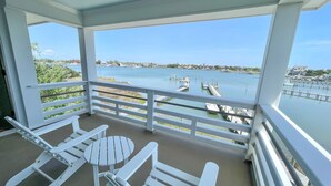 Een balkon met witte meubels, uitzicht op een jachthaven en een heldere lucht.