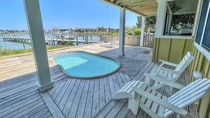 Een houten terras met een jacuzzi, witte Adirondack-stoelen en uitzicht op een jachthaven.