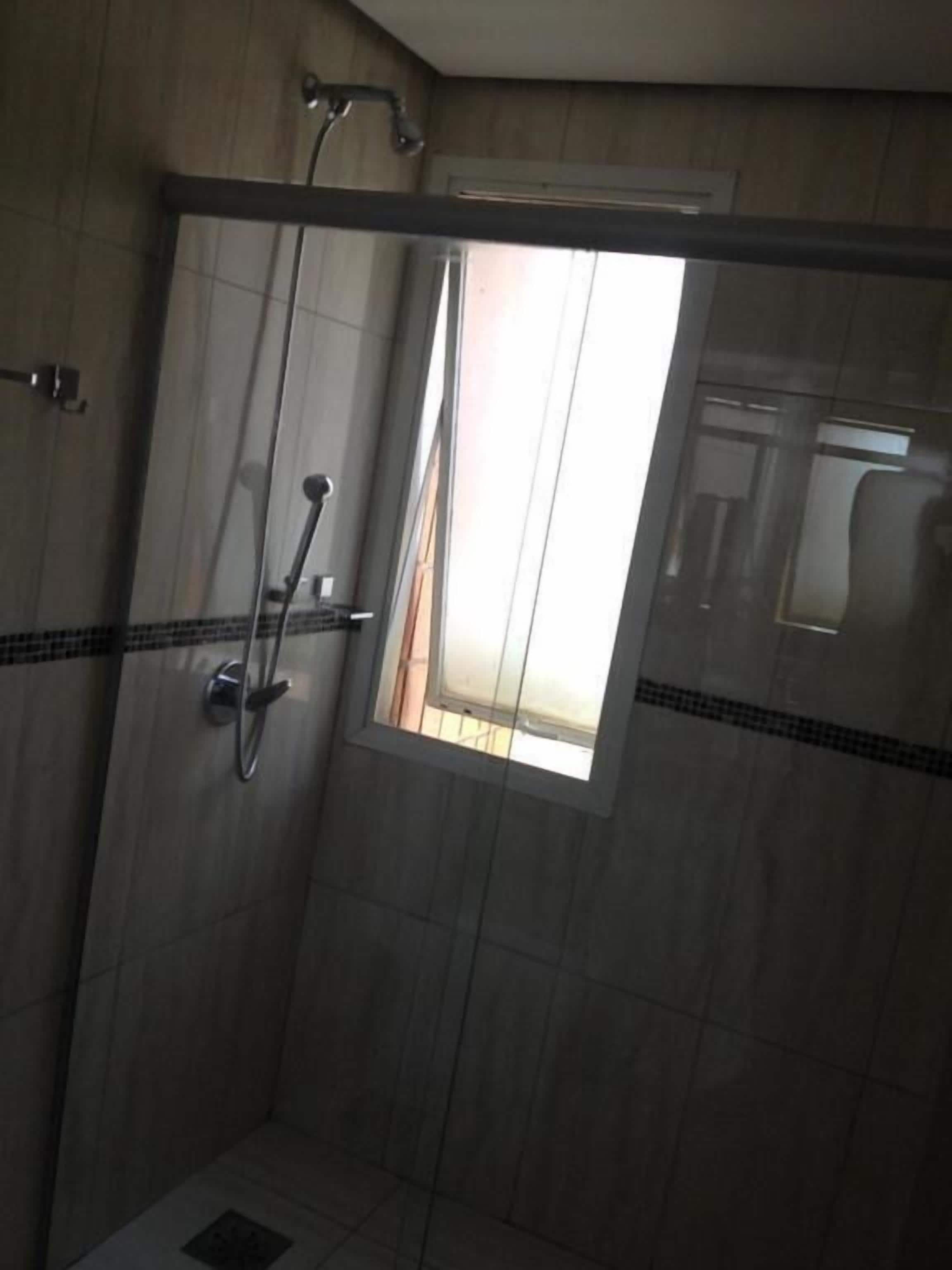 Ducha con puerta de vidrio, una ventana pequeña y pared de azulejos.