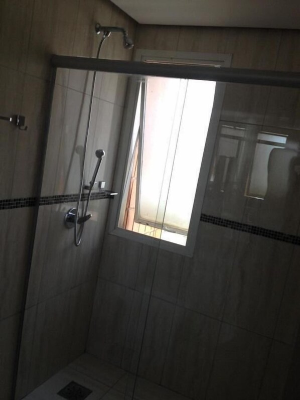 A shower with a glass door, a small window, and a tiled wall.
